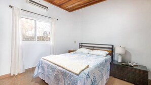 A bedroom with a bed, a bedside table, a lamp, and a window with curtains. - Tropical Sunset at Sunset Villas in West End, 2 bd Condo  (West End)