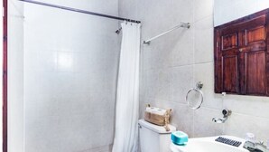 A bathroom with a toilet, a shower with a curtain, a sink with a mirror, and a wooden cabinet. - Tropical Sunset at Sunset Villas in West End, 2 bd Condo  (West End)