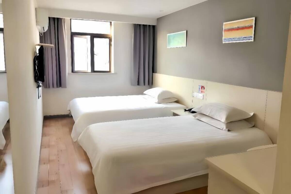 A hotel room with two beds, a window with curtains, a painting on the wall, and a wooden floor.