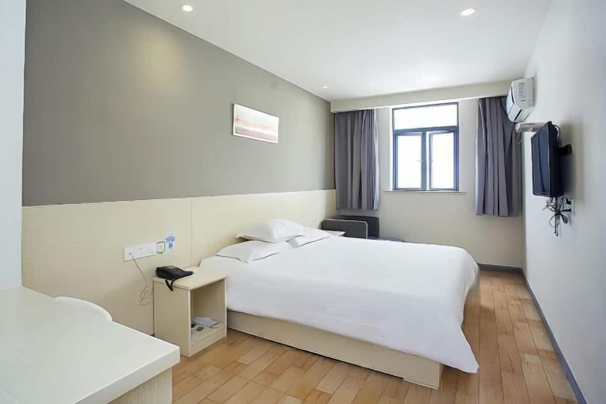 A hotel room with a bed, bedside table, and a window with curtains.