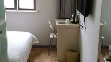 A bedroom with a bed, a desk with a kettle, a chair, and a waste bin.