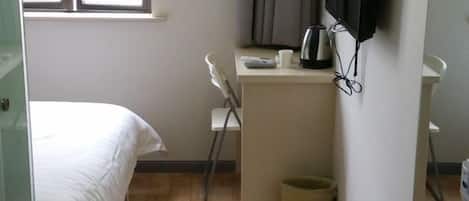 Une chambre avec un lit, un bureau avec une bouilloire, une chaise et une poubelle.