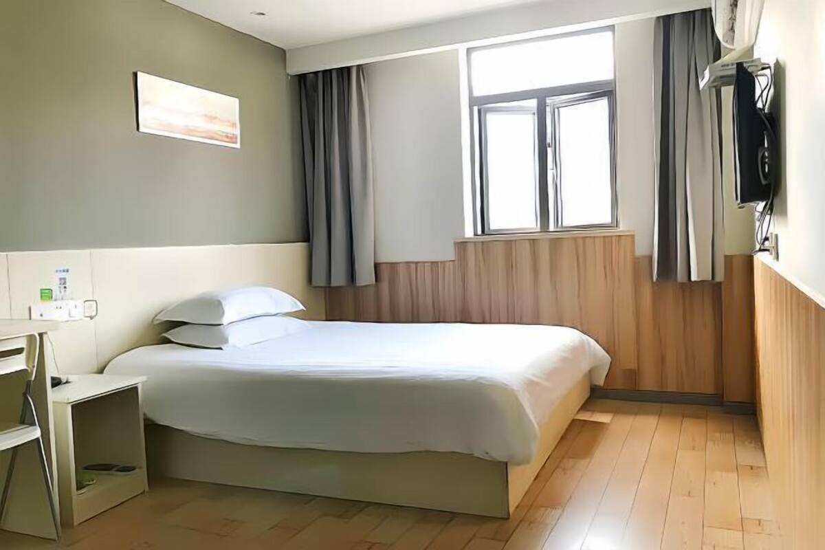 A hotel room with a bed, a desk, a window, and a TV.