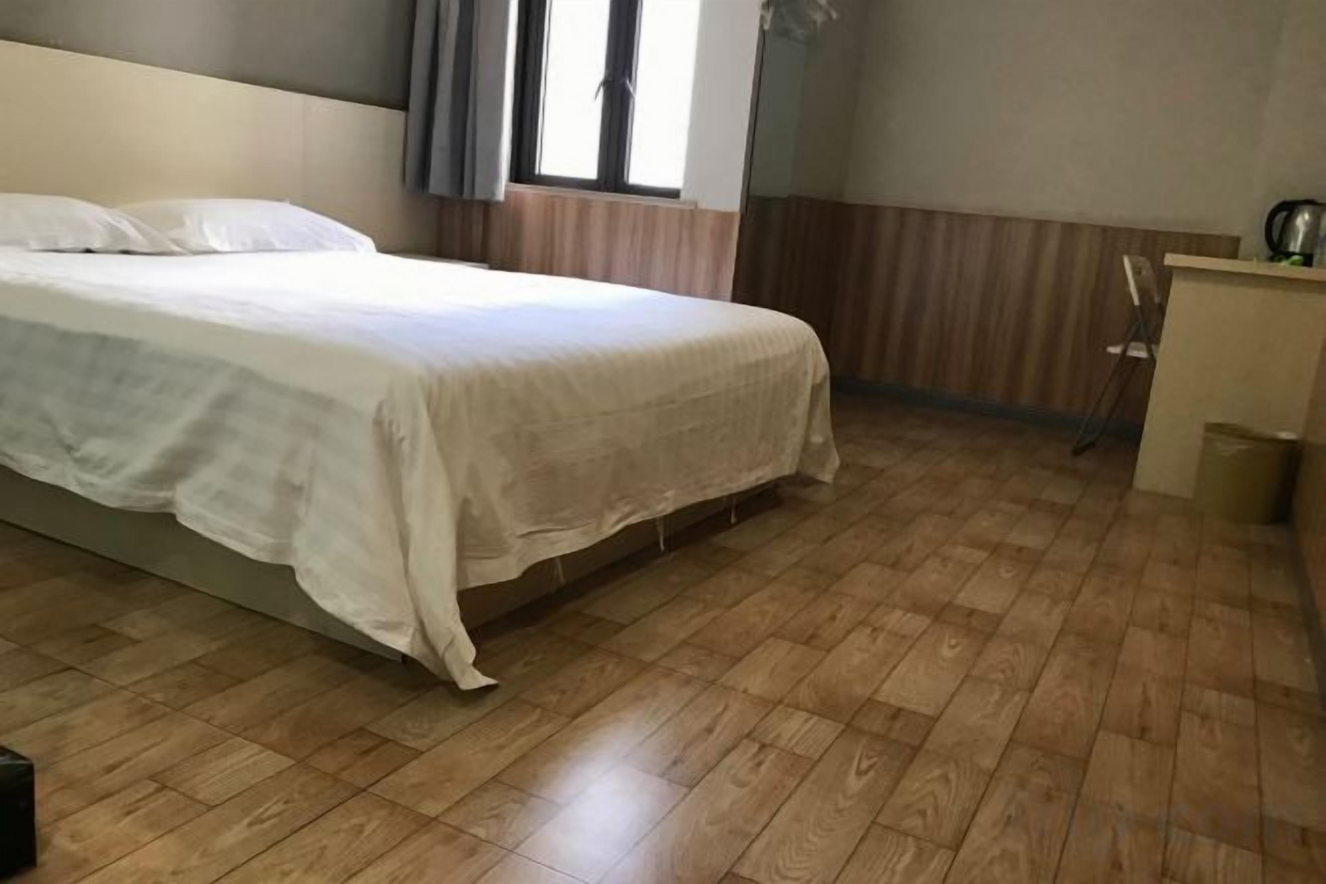 Une chambre à coucher avec un lit, un plancher en bois, une fenêtre avec des rideaux et un petit bureau avec une chaise.