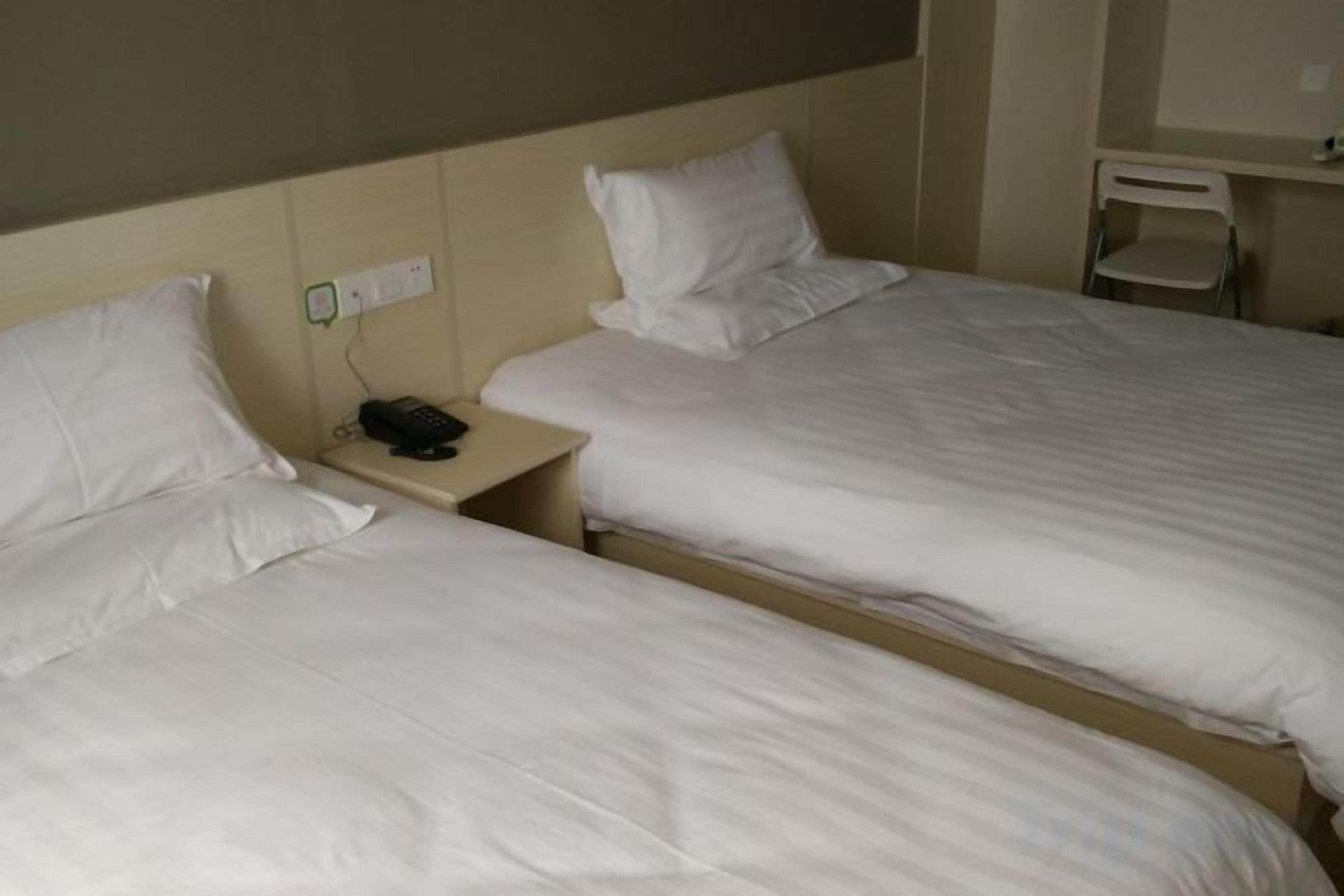 Two single beds with white linens, a bedside table with a phone, and a wall socket.
