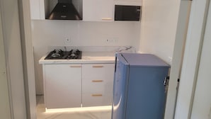 A compact kitchen with white cabinets, a black range hood, a microwave, and a blue refrigerator. - A cozy 3 BR apartment, 100m away from the beach and in a gated secured location. (IKATE - LEKKI)