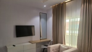 Una habitación de hotel moderna con una televisión de pantalla plana montada en la pared, un escritorio de madera, un sillón cómodo y un amplio ventanal con cortinas.