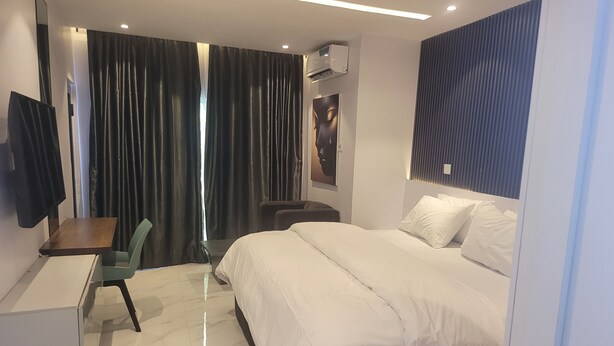 Una habitación de hotel moderna con cama, escritorio, silla y un amplio ventanal con cortinas.