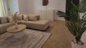 Una sala de estar con un sofá color beige, una mesa de centro redonda, una planta en maceta y un espejo grande en la pared.