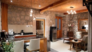 A modern kitchen with a stone wall, wooden ceiling, and a central island with chairs. - Casa Serdán Suites & Events (Morelia)