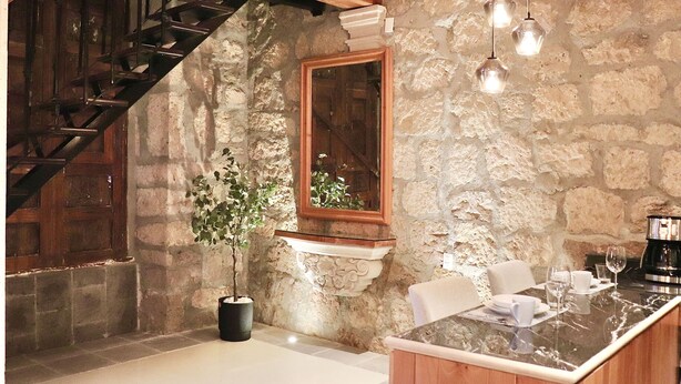 A stone-walled room with a wooden staircase, a potted plant, a marble bar area, and a coffee machine. - Casa Serdán Suites & Events (Morelia)