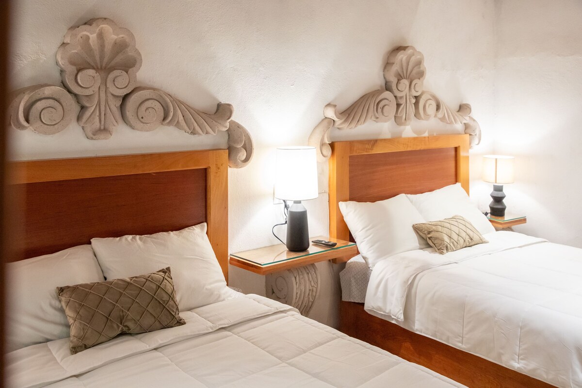 Two beds with wooden headboards, white bedding, and bedside tables with lamps.