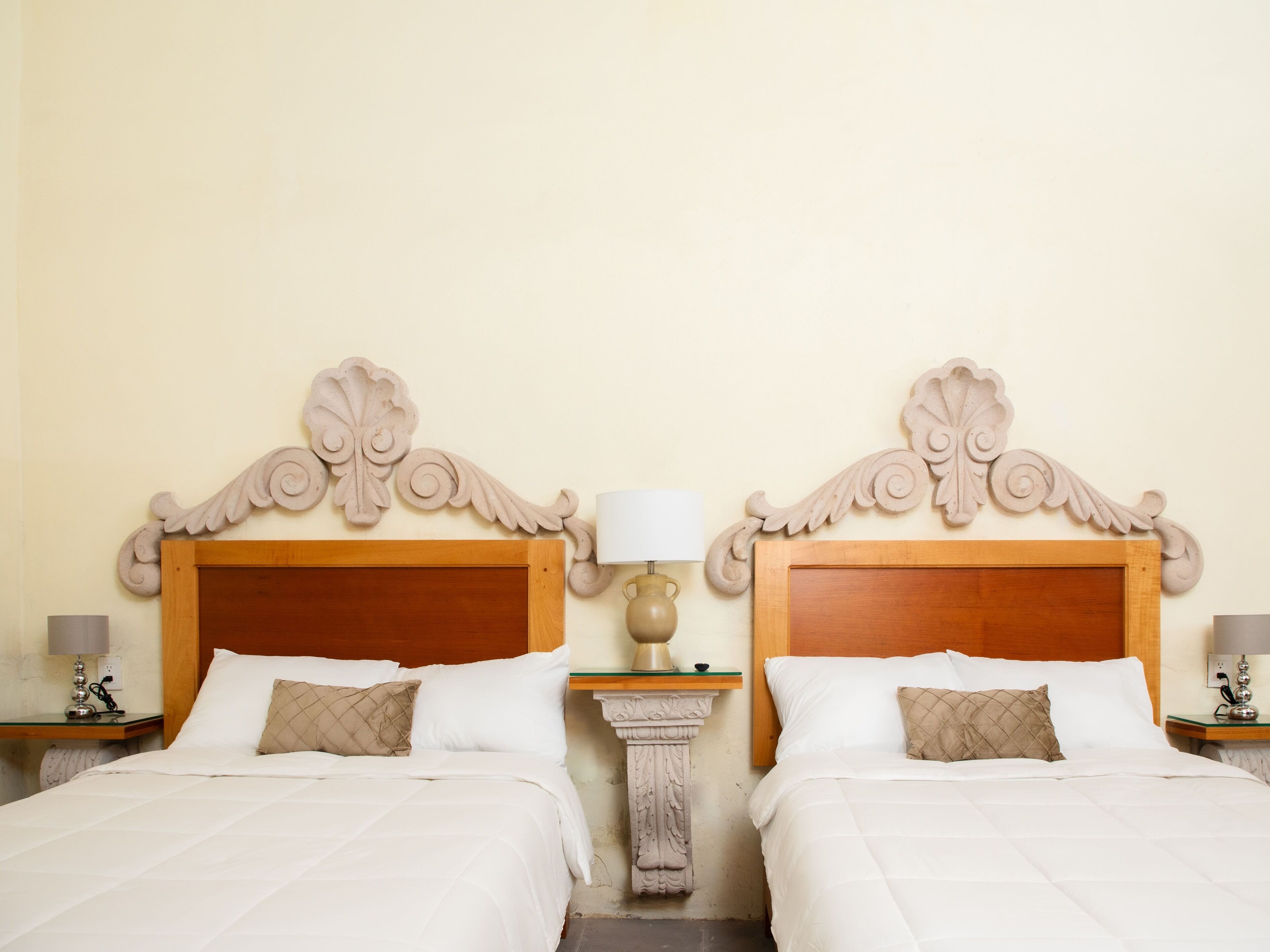 A hotel room with two beds, each with a wooden headboard and white bedding.