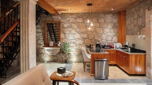 A kitchen with a stone wall, wooden cabinets, and a stainless steel refrigerator. - Casa Serdán Suites & Events (Morelia)