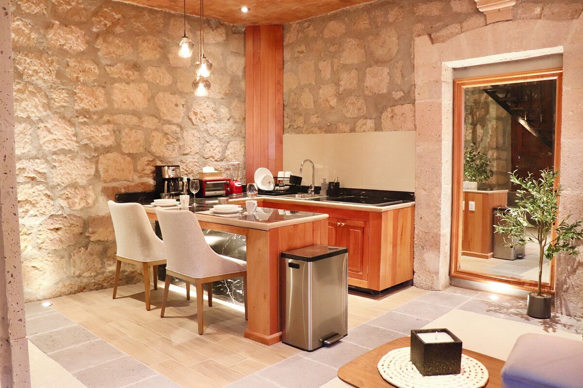 A compact kitchen with a stone wall, wooden cabinets, and a dining area with chairs.