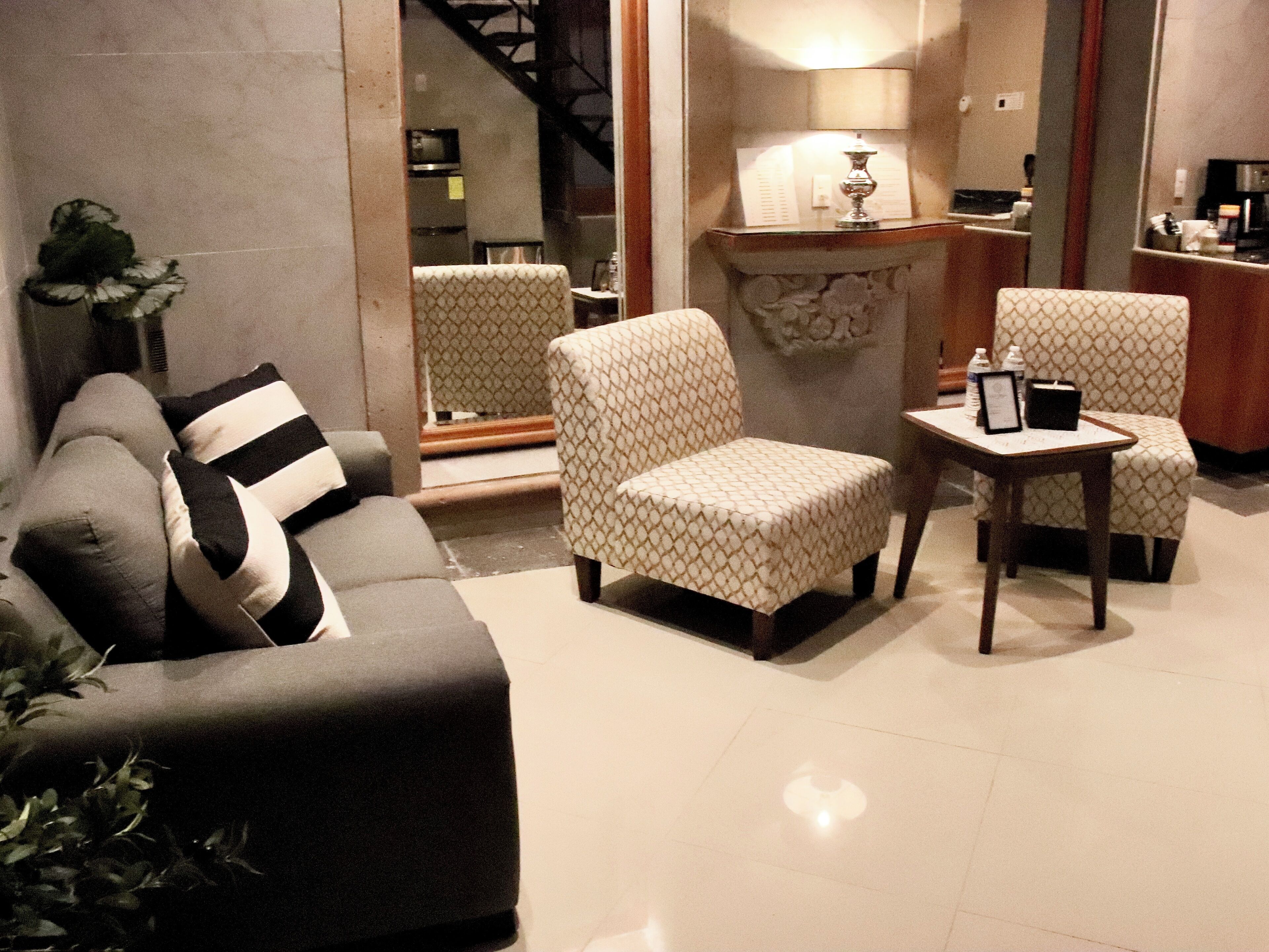 A living room with a sofa, two patterned armchairs, a small table, and a lamp.
