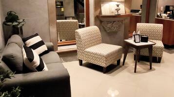 A living room with a sofa, two patterned armchairs, a small table, and a lamp.
