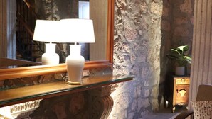 A stone-walled room with a large mirror, a glass table with two lamps, a wooden bench, and a potted plant. - Casa Serdán Suites & Events (Morelia)