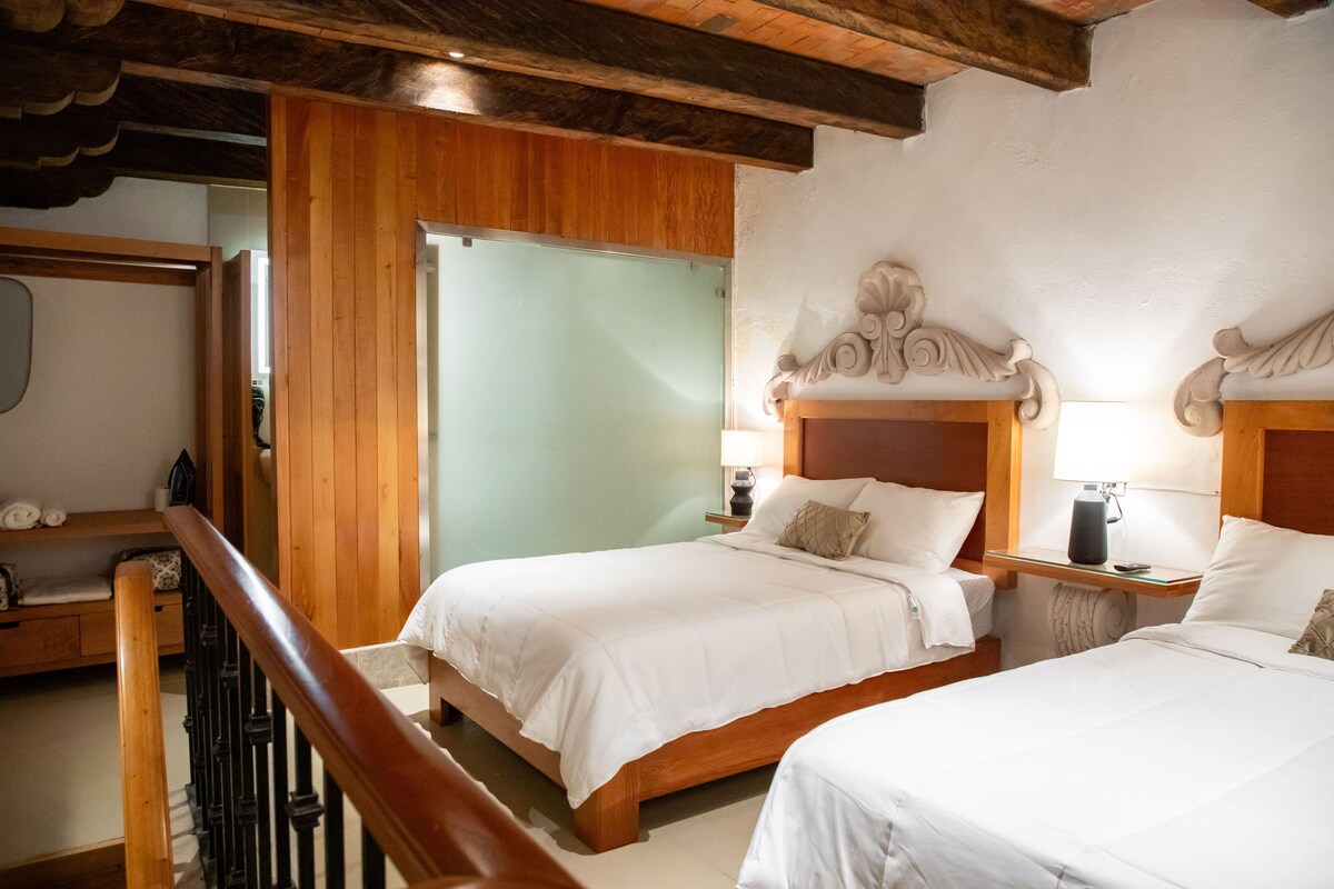 A hotel room with two beds, wooden headboards, a wooden staircase, and a wooden railing.