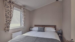Un dormitorio con cama, cortinas, una mesita de noche y una ventana.