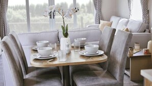 Un comedor con una mesa redonda dispuesta para cuatro personas, rodeada de sillas grises con tapicería. Un jarrón con flores blancas está sobre la mesa, y hay varios cuencos y vasos blancos.