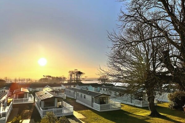 A row of mobile homes with white exteriors and balconies, situated near a body of water with a clear sky.