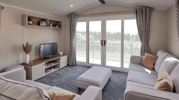 Una sala moderna con sofá, reposapiés, televisor y puerta corrediza de vidrio que da a un balcón.