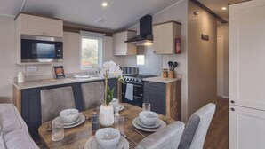 Cocina compacta con microondas, estufa y horno. Hay una mesa de comedor con sillas y un florero con flores.