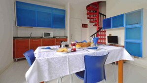 A dining area with a table set for two, a kitchen in the background, and a red spiral staircase. - Holiday apartment with air conditioning, balcony and pool (Lignano Sabbiadoro)