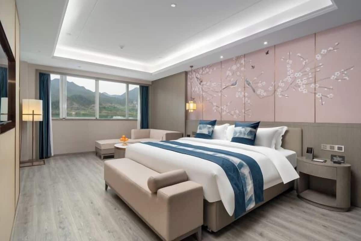 Une chambre d’hôtel moderne, dotée d’un grand lit, d’un canapé, d’une table de chevet et offrant une vue sur les montagnes par la fenêtre.