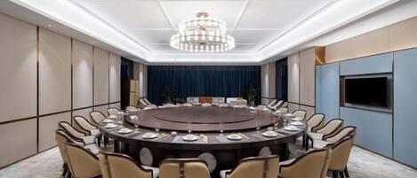 Un salón de conferencias con una mesa redonda, sillas y una araña.