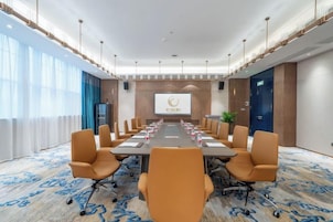 Un salón de conferencias con una larga mesa, varias sillas, una pantalla de proyector y un amplio ventanal.