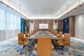 A conference room with a long table, multiple chairs, a projector screen, and a large window.
