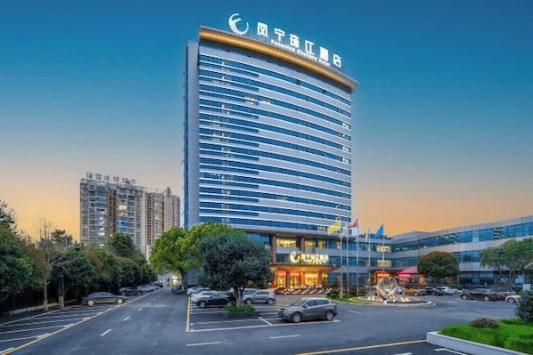A modern hotel with a curved facade, multiple floors, and a parking lot in front. - Fengning Zhujiang Hotel (Xiushui)