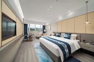 A modern hotel room with a large bed, a desk, and a view of the mountains.