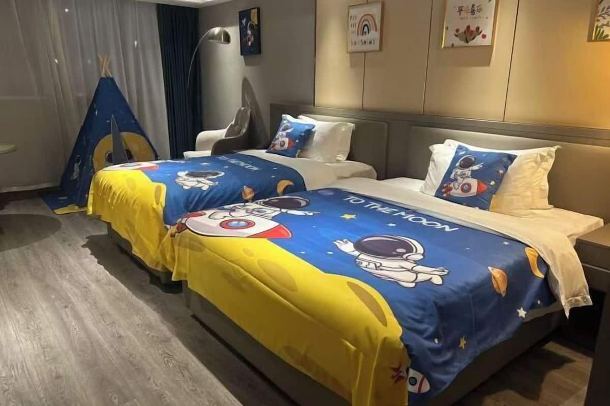 Une chambre d’hôtel avec deux lits, chacun étant agrémenté d’une couvre-lit sur le thème de l’espace. Un élément décoratif en forme de tente se trouve sur le côté gauche de la pièce.
