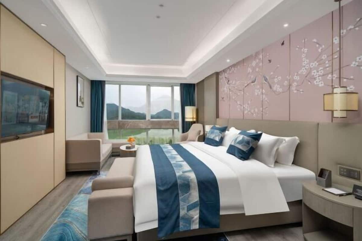 Une chambre d’hôtel moderne dotée d’un grand lit, d’un canapé, d’un bureau et offrant une vue sur les montagnes par la fenêtre.