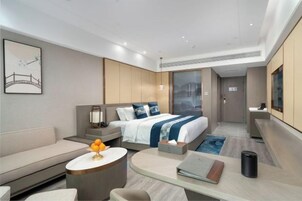 A modern hotel room with a bed, a sofa, a desk, and a small table.