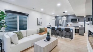 Una sala de estar moderna con un sofá, una mesa de centro y una zona de cocina con taburetes de bar.