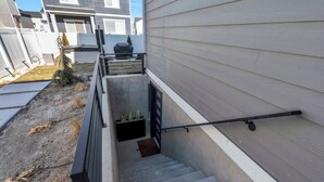 Una escalera residencial con barandilla metálica, rellano de concreto y una pequeña maceta con plantas.
