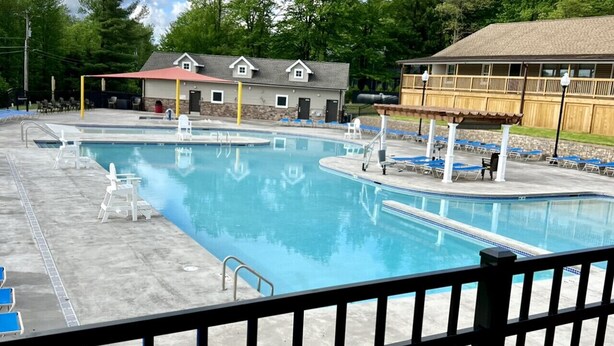 A swimming pool with blue lounge chairs and a covered area, surrounded by buildings and trees. - Poconos Gem • Hot Tub • Near All Attractions (Tobyhanna)