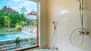 A bathroom with a freestanding bathtub, a shower, and a view of a swimming pool and garden. - Villa Sri Rejeki (Ubud)