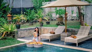 A poolside area with lounge chairs, a decorative umbrella, and potted plants. - Villa Sri Rejeki (Ubud)