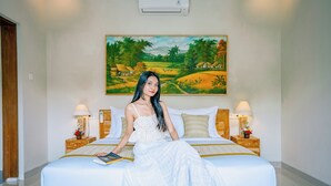 A bed with a painting of a landscape, a lamp, and a book on the bed. - Villa Sri Rejeki (Ubud)