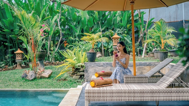 A poolside area with a lounge chair, a large umbrella, and lush greenery in the background. - Villa Sri Rejeki (Ubud)