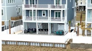 A two-story beachfront house with a balcony, outdoor seating, and a view of the water. - New Lagoon-Front Beach Home w/ Private Pool, Elevator, & Oceanfront Pool Access (Ocean Isle Beach)