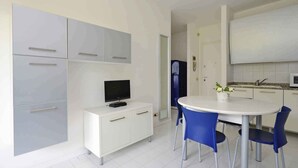 Eine moderne Küche mit weißen Schränken, einem Esstisch mit blauen Stühlen und einem Fernseher auf einem weißen Schrank.