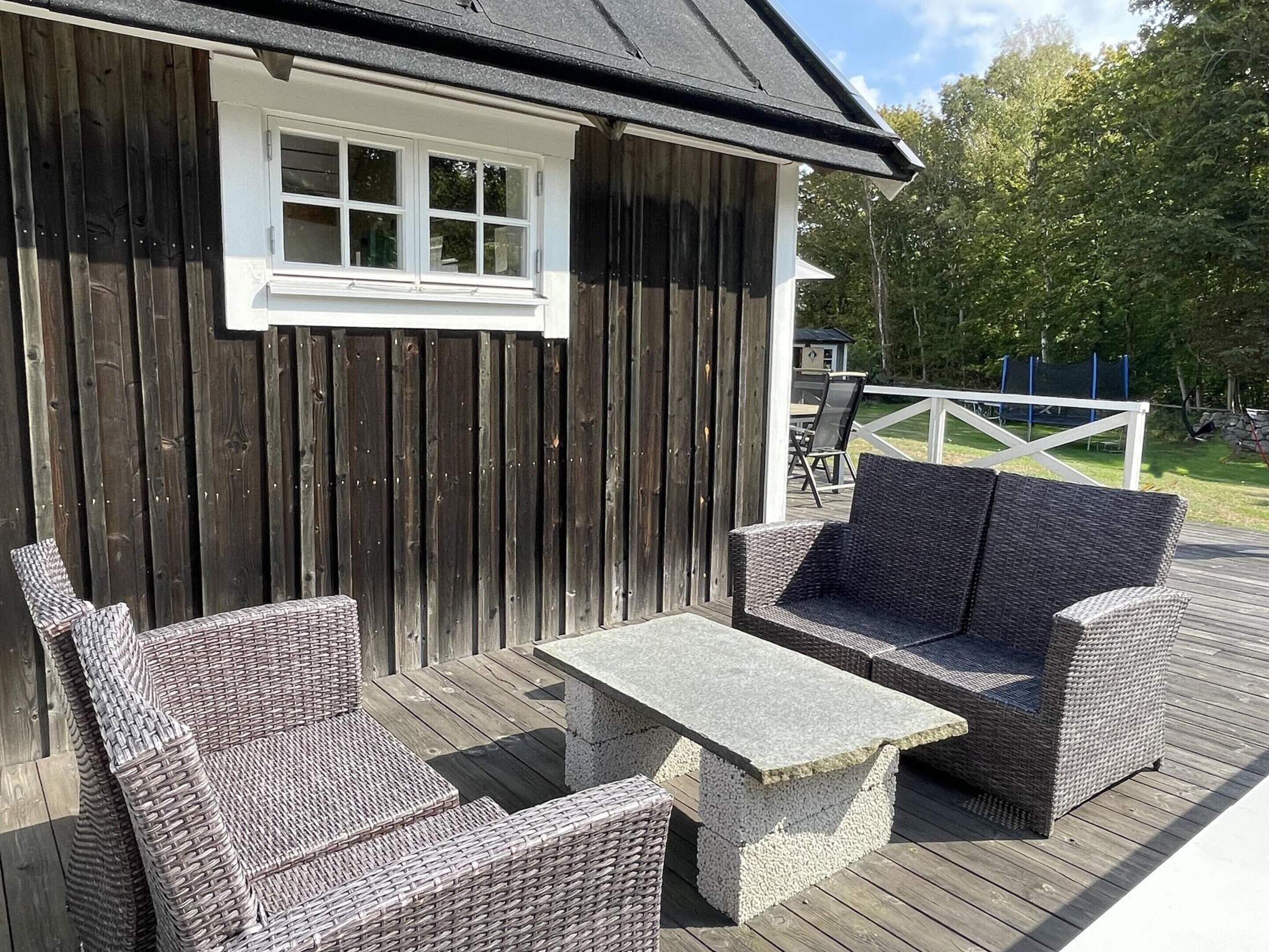 Une terrasse en bois avec des meubles en osier, notamment deux chaises et une table.