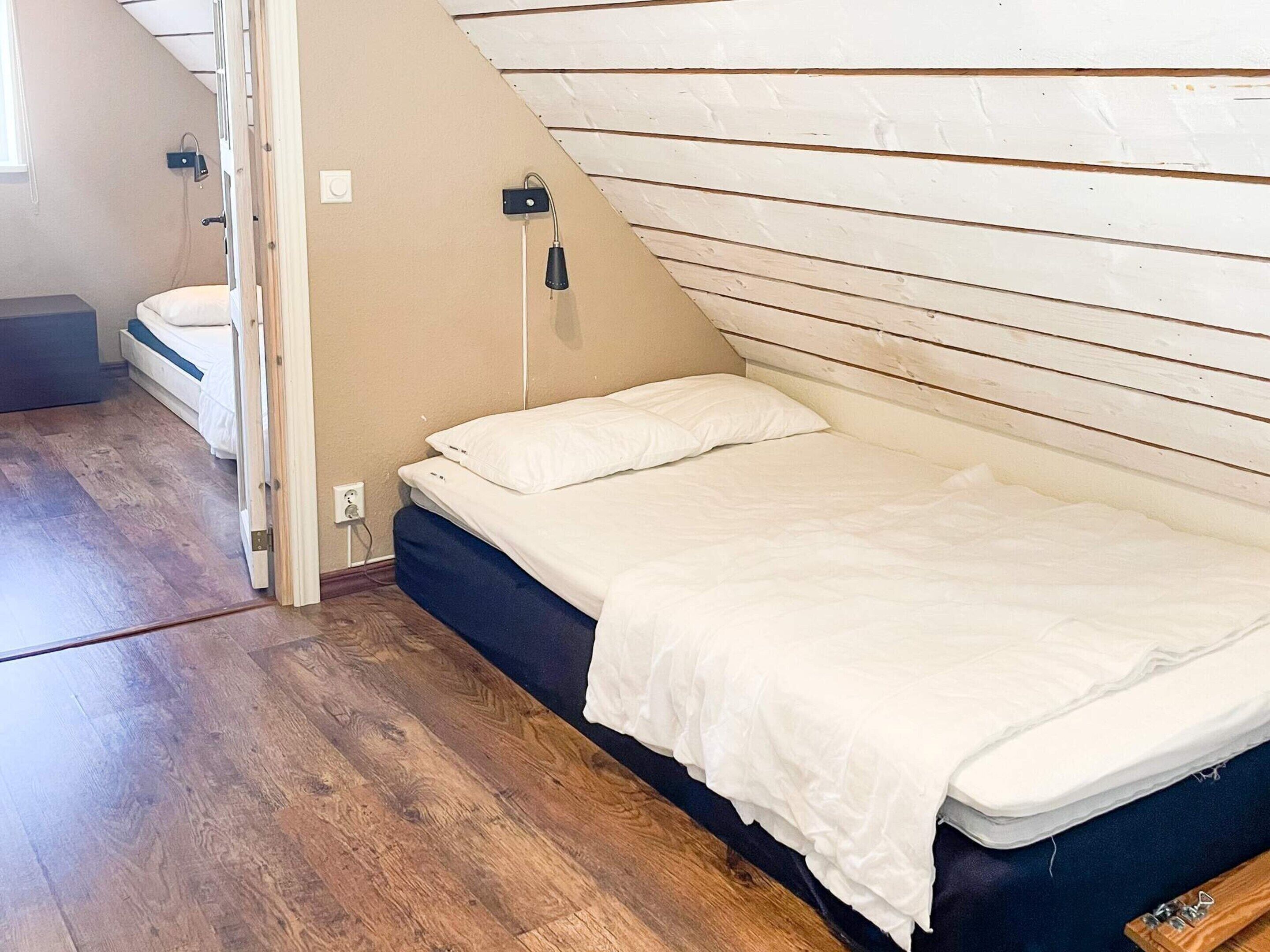 Una cama individual en una habitación con techo inclinado, suelo de madera y una mesita de noche pequeña.