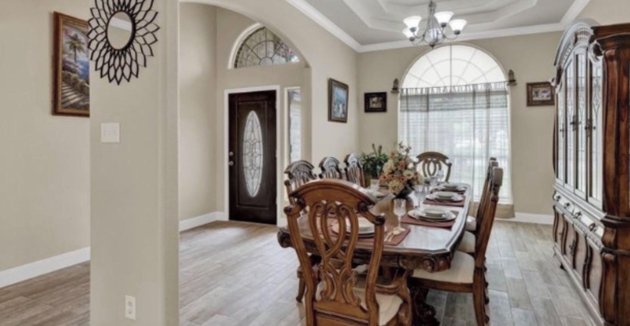 Comedor con mesa y sillas de madera, una araña y un aparador grande de madera con puertas de cristal.